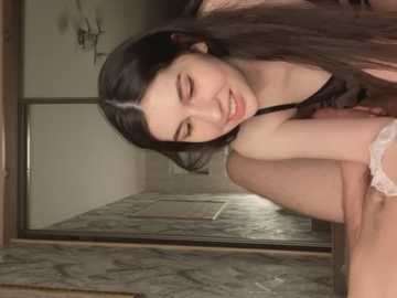 Media: Video of a young woman with long black hair, wearing a black lace bra, leaning over a marble counter, smiling softly, in a dimly lit room.