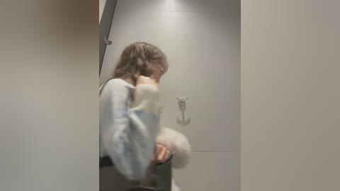 Media: A blurred video of a person in a light blue sweater and white pants holding a fluffy white dog in a modern, minimalist hallway with gray walls.