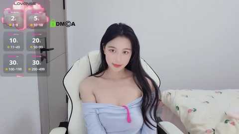 Media: Video of an East Asian woman with long black hair, fair skin, and red lipstick, seated in a white gaming chair, wearing a light blue off-shoulder top.