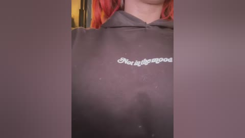 Media: Video of a person with red hair, wearing a dark hoodie with \"Sorority Dropout\" printed on it, partially obscured by a blurry background.