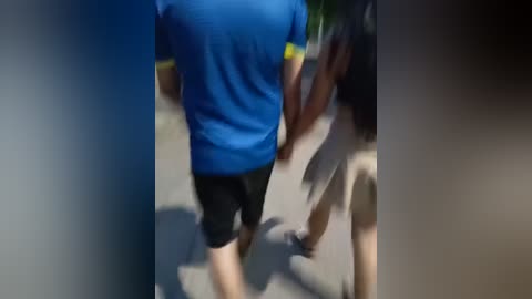 Media: A blurred video shows a person in a blue T-shirt and black shorts walking away, with a person in a black shirt and beige shorts following. The background is indistinct.