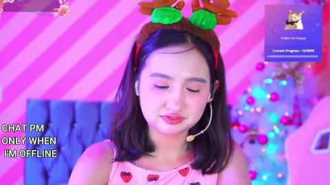 Media: Video of a young Asian woman with shoulder-length black hair, wearing a Santa hat and strawberry-patterned dress, smiling against a pink, striped background, with text overlay \"CHAT PM ONLINE\" in white.