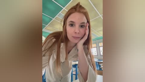 Media: Video of a young, fair-skinned woman with long, straight red hair, wearing a beige cardigan, leaning on her hand, in a brightly lit, retro diner with green and white ceiling tiles.