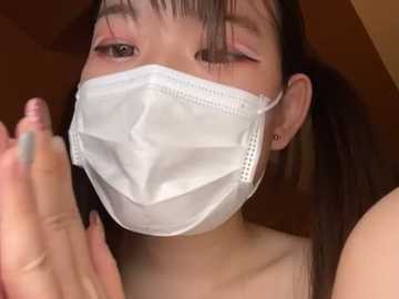 Media: Video of an East Asian woman with light skin and long, straight black hair. She wears a white surgical mask, pink eyeshadow, and winks. Background is blurred, suggesting an indoor setting.