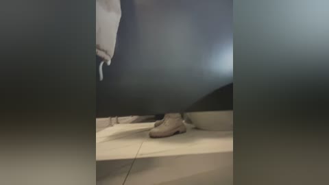 Media: A blurry video shows a person in beige shoes and pants standing on a white tiled floor in a dimly lit bathroom, partially obscured by a dark, blurry window.