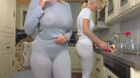 Media: Video of two women in matching white athletic gear, one washing dishes in a modern kitchen, the other seated on a fancy chair.