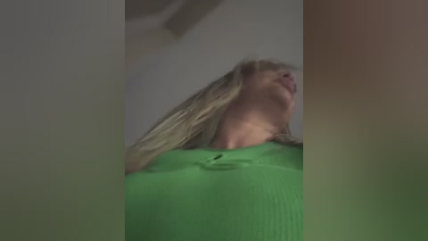 A blurry video shows a young woman with long blonde hair, wearing a bright green shirt, captured from a low angle, with a slightly out-of-focus background.