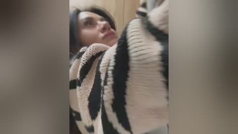 Media: Video of a woman with long, dark hair, wearing a thick, striped knit sweater, looking slightly confused or startled, with blurred, vertical edges suggesting a fisheye lens effect.