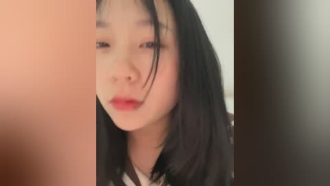 Media: Video of a young Asian woman with fair skin, straight black hair, and red lipstick, partially obscured by a blurred, dark object on the right.