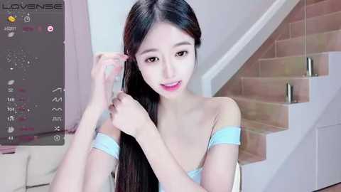 Media: Video of a young Asian woman with long black hair, fair skin, and small breasts, smiling while brushing her hair. Background shows a white wall and a staircase.