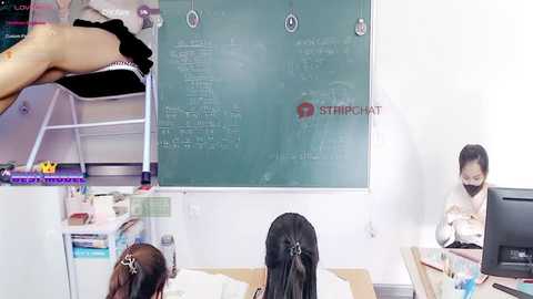 Media: Video of a classroom with a teacher on a ladder writing on a green chalkboard, students at desks, and a monitor on the right.