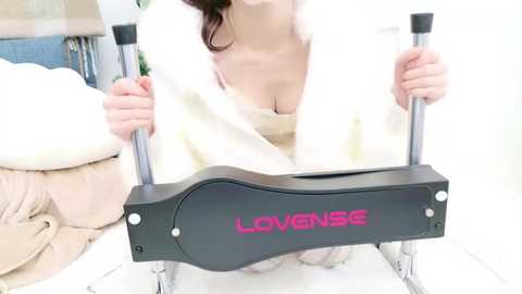 Media: Video of a woman with long, dark hair, partially wrapped in a white towel, using a black, ergonomic \"LONGENSE\" hand exerciser. The background features a white wall and a plush, beige couch.