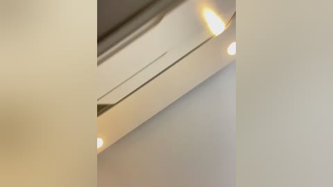 Media: A close-up video of a ceiling with a smooth, light beige finish and three small recessed lights emitting a soft, warm glow. The image captures a clean, modern interior design with minimalistic aesthetics.