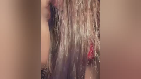 Media: Video of a close-up of a person with long, wet, blonde hair, partially covering their face, with a red mark visible on the cheek. The background is blurred and neutral-toned.