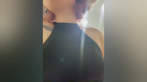 Media: Video of a woman with curly, light brown hair, wearing a black halter top, with a blurred background. The image has a soft, vintage filter, emphasizing the woman's curves and the texture of her hair.