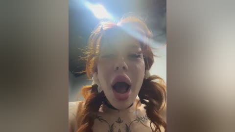 Media: Video of a fair-skinned woman with red pigtails, wearing a black choker and floral tattoos, mouth open in a dramatic expression, lens flare in the background.