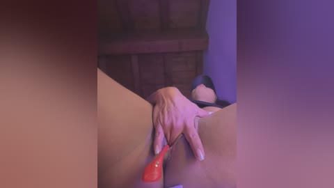 Media: A video captures a woman's hand inserting a red vibrator into her vagina, her face obscured. The background features a wooden ceiling and purple wall.