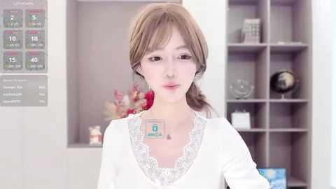 Media: A video of a young Asian woman with light skin, straight brown hair, and a white lace-trimmed top. She stands in a modern, minimalist office with white walls, a desk, and a digital clock.