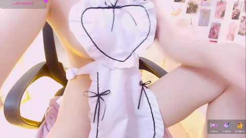 Media: Video of a fair-skinned woman wearing a revealing white maid outfit with a heart-shaped cutout, revealing her breasts, sitting on a black office chair in a softly lit room.