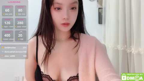 Media: Video of a young East Asian woman with long black hair, fair skin, and a slender physique, wearing a black lace bra. Background includes a white wall and a pink towel draped over her shoulder.