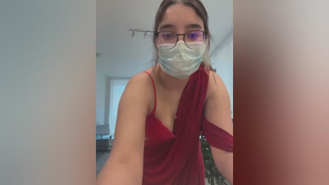 Media: A video of a young woman with glasses and a mask, wearing a revealing red dress, standing in a modern kitchen.