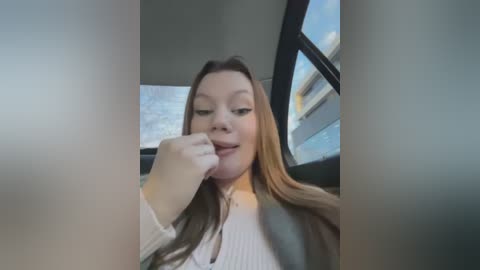 Media: Video of a young Caucasian woman with long, straight, blonde hair, wearing a white sweater, smiling and biting her finger in the car's passenger seat.