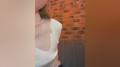 Media: A video captures a close-up of a person in a white, textured top against a brick wall, with a blurred background. The image is slightly out of focus.