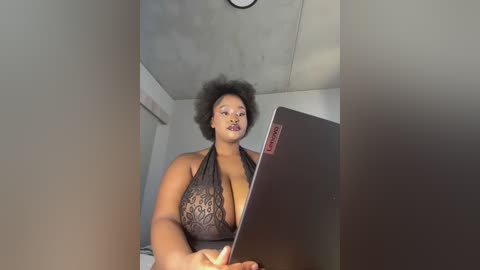 Video of a plus-sized Black woman with large breasts, wearing a revealing black lace halter top, sitting at a desk, typing on a laptop.