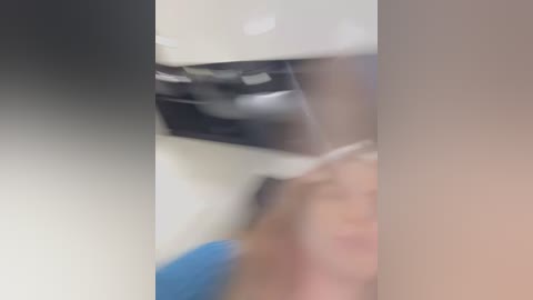 Media: Blurry video of a person's face and arm, possibly in a hospital setting, with a blue object and white walls in the background.