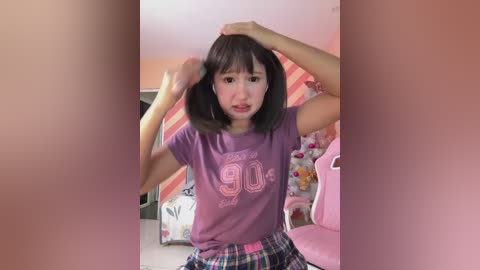 Media: Video of an Asian woman with straight black hair, medium build, wearing a purple t-shirt and plaid pants, adjusting her hair in a pink room with floral wallpaper and a pink chair.