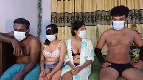 Media: Video of four shirtless South Asian men in face masks, two in floral tops, sitting on a green couch, with yellow curtains in the background.