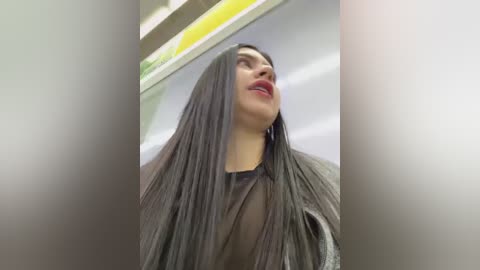 Media: Video of a woman with long, straight, dark hair, wearing a black, shiny hair cap, standing in a modern, well-lit salon with a yellow and green ceiling.