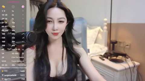 Media: A video shows an Asian woman with long black hair and fair skin, wearing a low-cut black top, sitting in a bedroom. She is using a microphone, and the room has a bed and nightstand with a lamp.