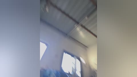 Video of a dimly lit room with a metallic ceiling and white walls. The image is blurry, possibly due to camera shake or motion, and features indistinct shapes and objects in the background.