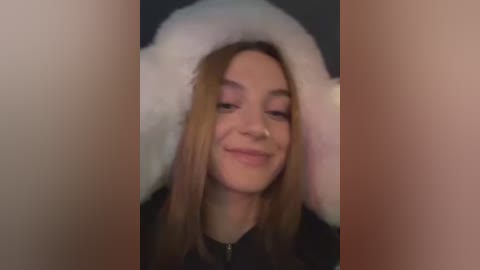 Media: A video of a young woman with light skin, straight blonde hair, and a white fur-trimmed hat, smiling. The background is blurred, and she is wearing a black jacket.