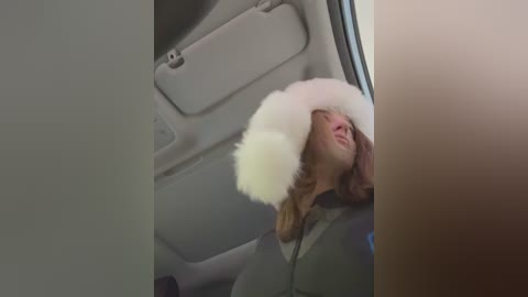 Media: Video of a person with shoulder-length, light brown hair wearing a white fur hat, visible through a car window, with gray interior visible.