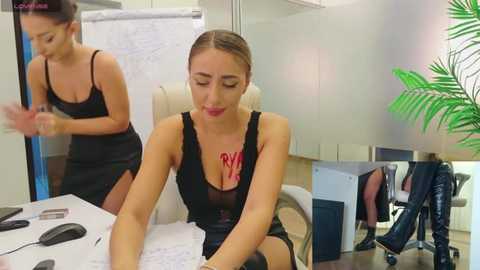 Media: Video of two women in an office: one with blonde hair, black dress, necklace, and red lipstick; the other with dark hair, black dress, and red lipstick, both focused on paperwork.