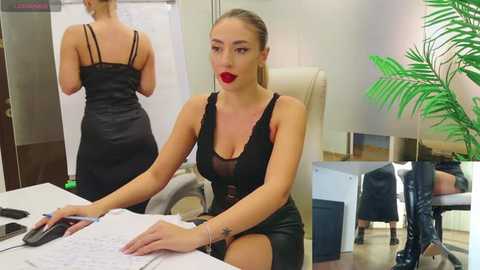 Media: Video of a blonde woman in a black, sheer, lace-trimmed dress, sitting at a desk, with a potted plant and a whiteboard in the background.