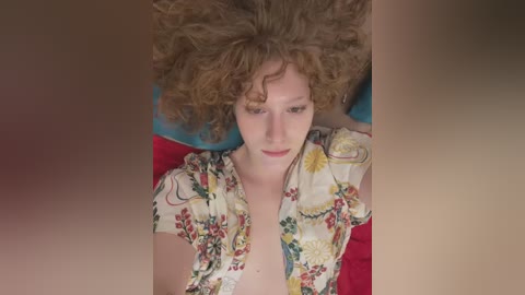 Media: A video of a young woman with curly red hair lying on a red pillow, wearing a floral blouse. She appears relaxed and serene.