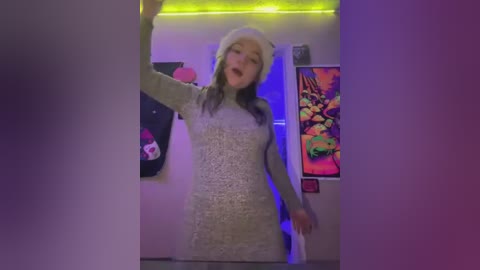 Media: Video of a young woman with light skin, long dark hair, and a gray knitted dress, wearing a white beanie, dancing in a dimly lit room with neon green lights, colorful posters, and a vibrant mural in the background.