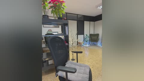 Media: A video of a minimalist, modern therapy room with beige walls, a black metal shelving unit, a black chair, a potted plant, and a cushioned massage chair.