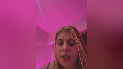 Media: Video of a young woman with wet, light brown hair, wearing a pink top, in a dimly lit room with pink neon lighting, giving a sultry, intimate atmosphere.