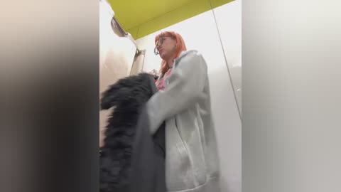 Media: A video captures a woman with red hair and glasses, wearing a light gray coat, holding a black, fluffy dog under a bright yellow umbrella in a dimly lit, narrow alleyway.