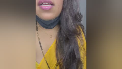 Media: A close-up video of a woman with medium brown skin, wearing a mustard-yellow blouse with a black choker, long dark wavy hair, and pink lipstick.