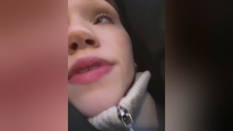 Media: Video of a close-up of a woman's face, focusing on her lips and chin. She has fair skin, pink lipstick, and a white fleece jacket. The background is blurred.