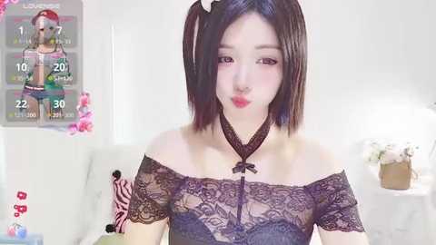 Media: Video of an Asian woman with short black hair, wearing a black lace off-shoulder top, sitting in a white room with a gaming overlay.