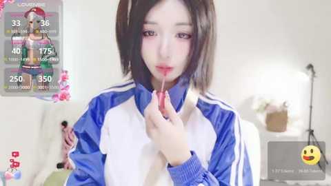 Media: Video of an Asian woman with straight black hair, wearing a blue and white track jacket, licking a lollipop in a bright, minimalist room.