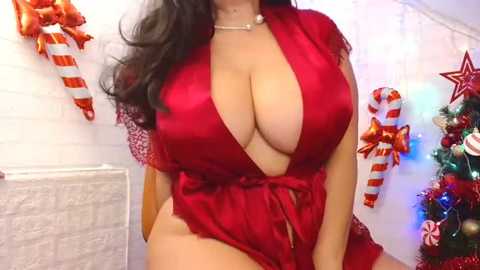 Media: Video of a curvaceous woman with long dark hair, wearing a revealing red satin robe with a deep V-neck, revealing ample cleavage. Background features holiday decorations: white stockings, striped candy canes, and a festive tree.