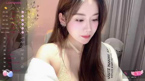 Media: Video of a young East Asian woman with fair skin, long brown hair, and a delicate, slender physique. She wears a white, off-shoulder top and a choker. Background includes a blurred indoor setting with soft lighting.