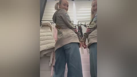 Media: Video of two women in a dressing room, one facing away, wearing a gray hoodie and blue jeans, the other in the mirror, holding hands.